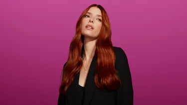 lady red hair standing agaisnt a pink background