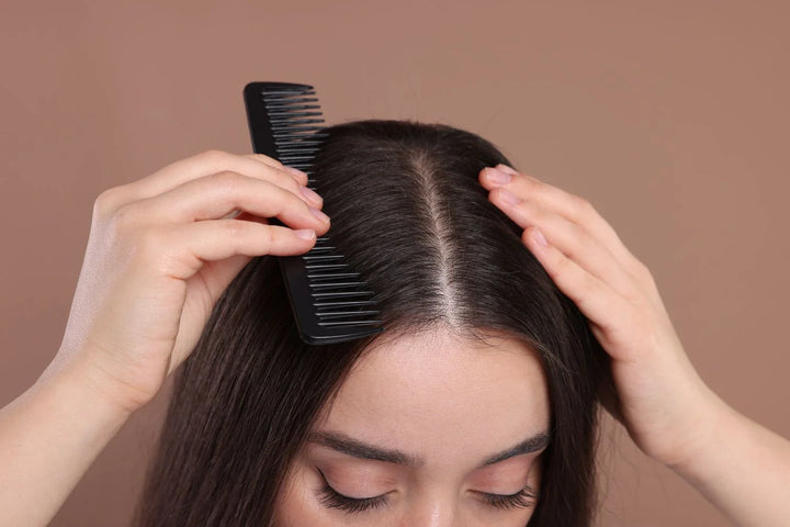 lady combingthrough her scalp with a fine tooth comb, top view, brown background