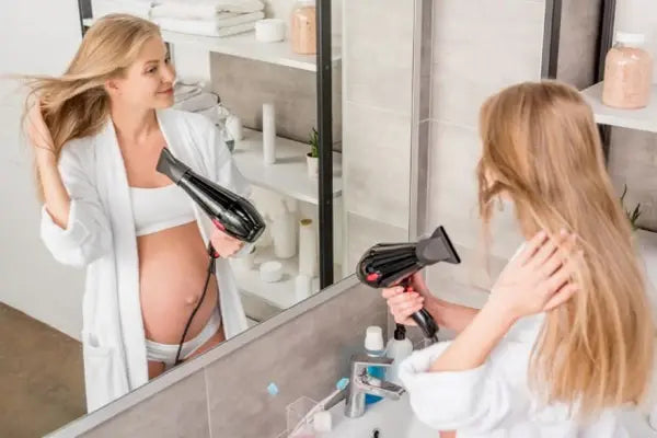 pregnant woman drying her hair in the mirrors