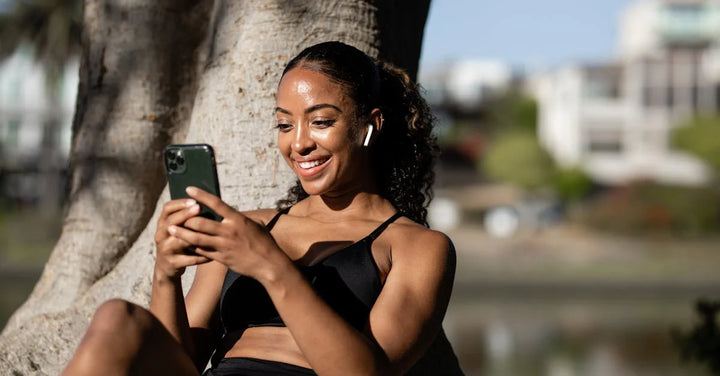 lady sitting under a tree smiling at her phone