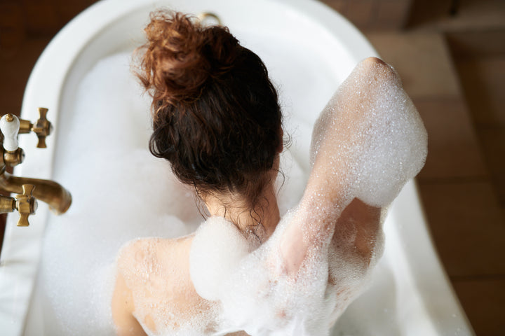 person scrubbing thei back with bubbles in a bath